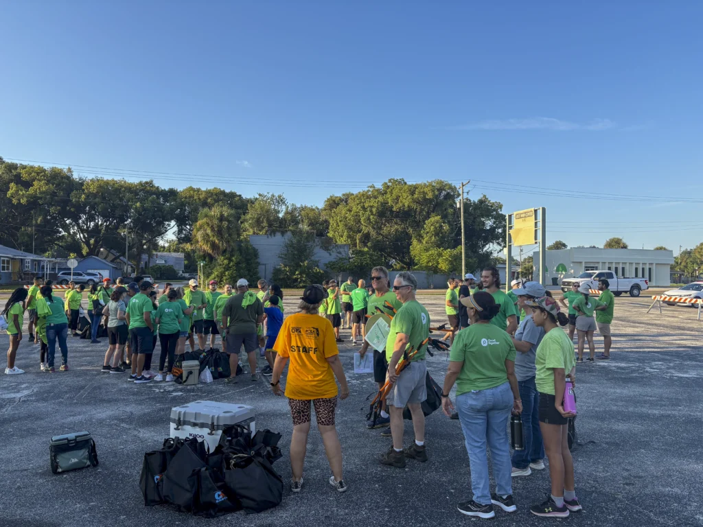 Large group of volunteers in green shirts gathering in a parking lot with litter grabbers at a Bartow CRA community cleanup