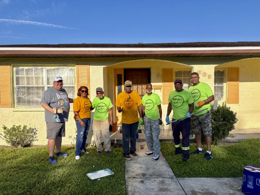 Impact volunteers posing in front of a freshly painted yellow home after a Bartow CRA neighborhood improvement project