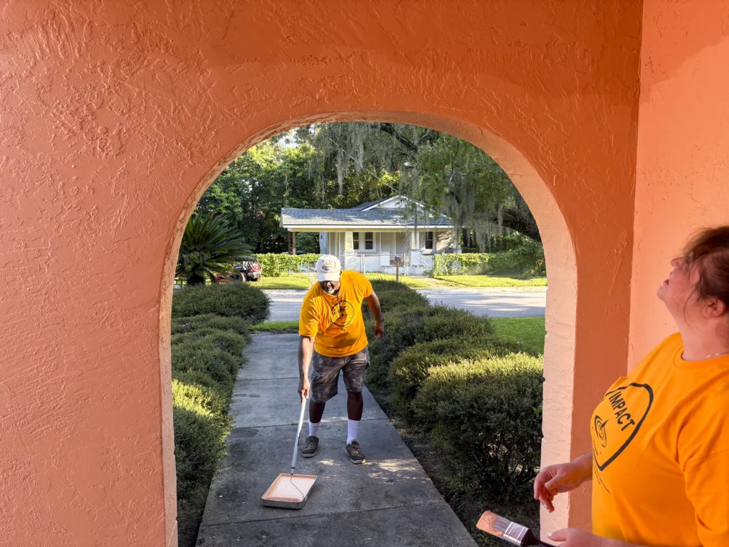 Volunteers painting the exterior of a Bartow home seen through an arched doorway during a CRA neighborhood improvement project