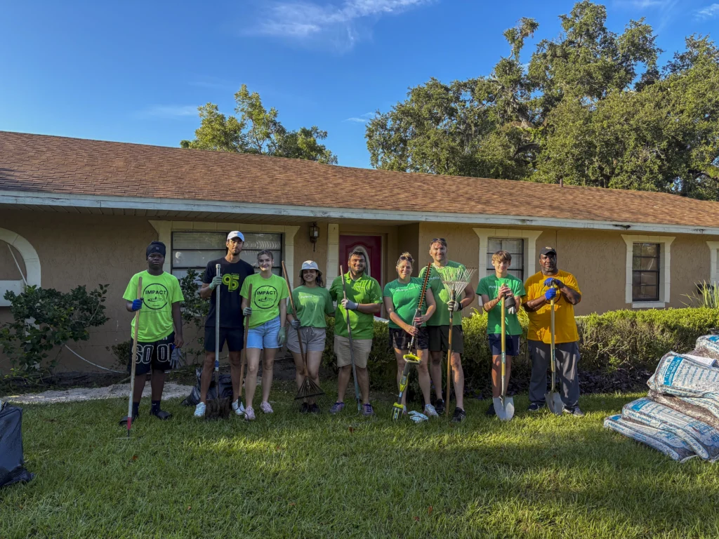 Large group of volunteers with yard tools posing in front of a Bartow home during a CRA community cleanup