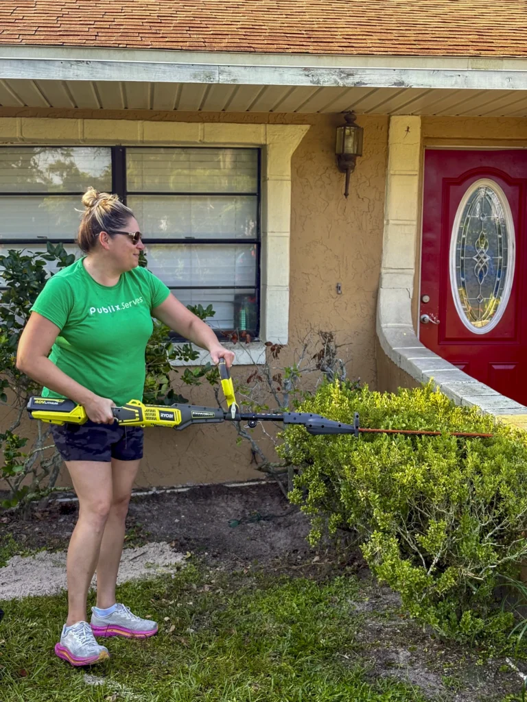 Publix Serves volunteer using a cordless hedge trimmer on shrubs in front of a Bartow home
