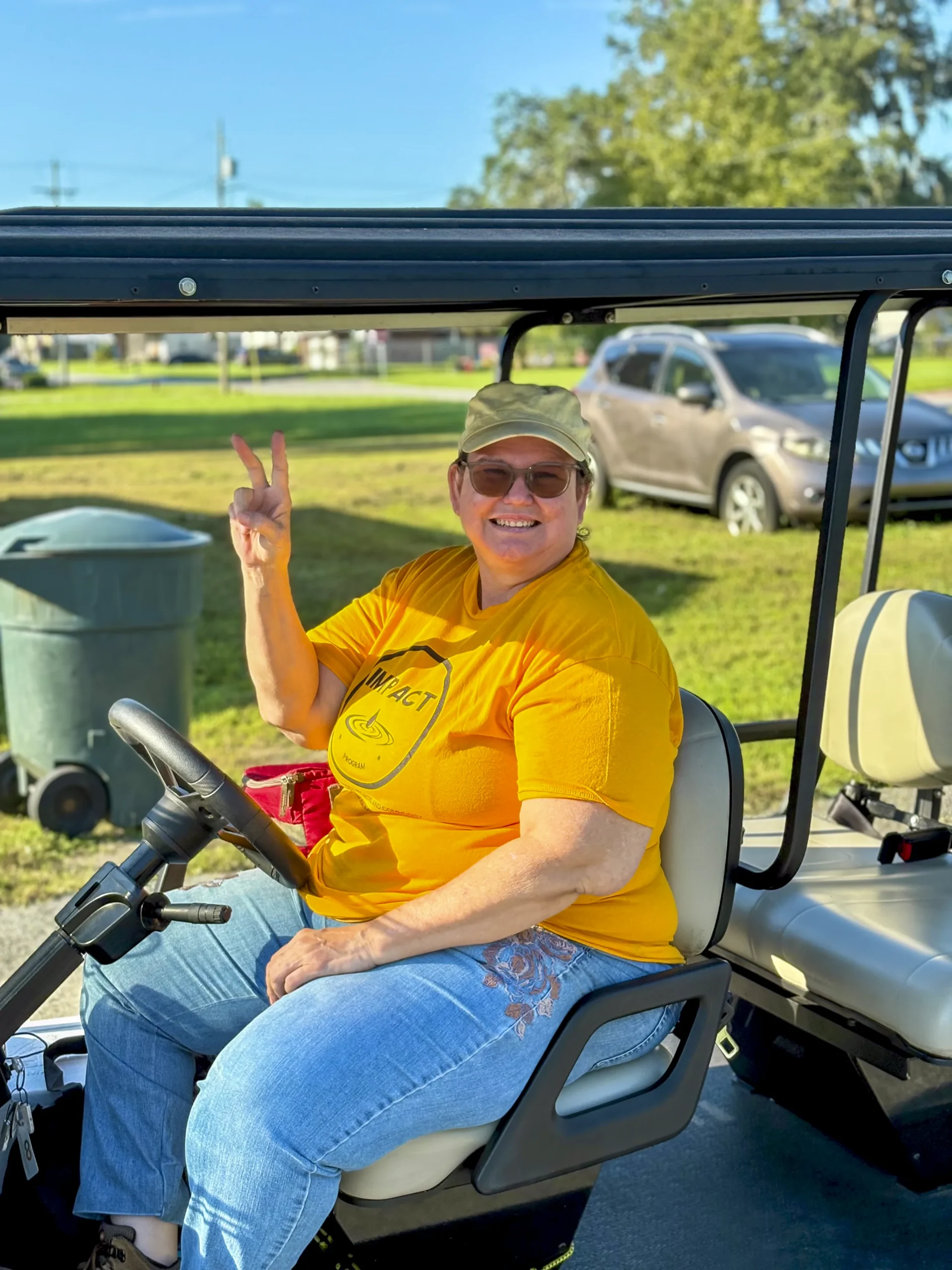 Smiling volunteer in a yellow shirt giving a peace sign while sitting in a golf cart at a Bartow community event