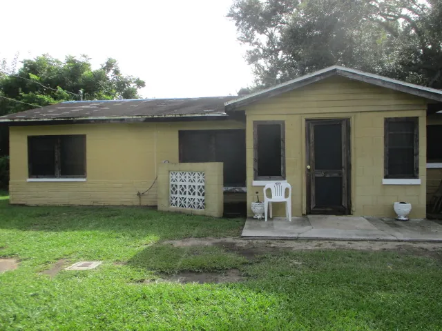 Before: single story yellow concrete block home with a worn, stained roof and damaged window frames prior to CRA funded rehabilitation
