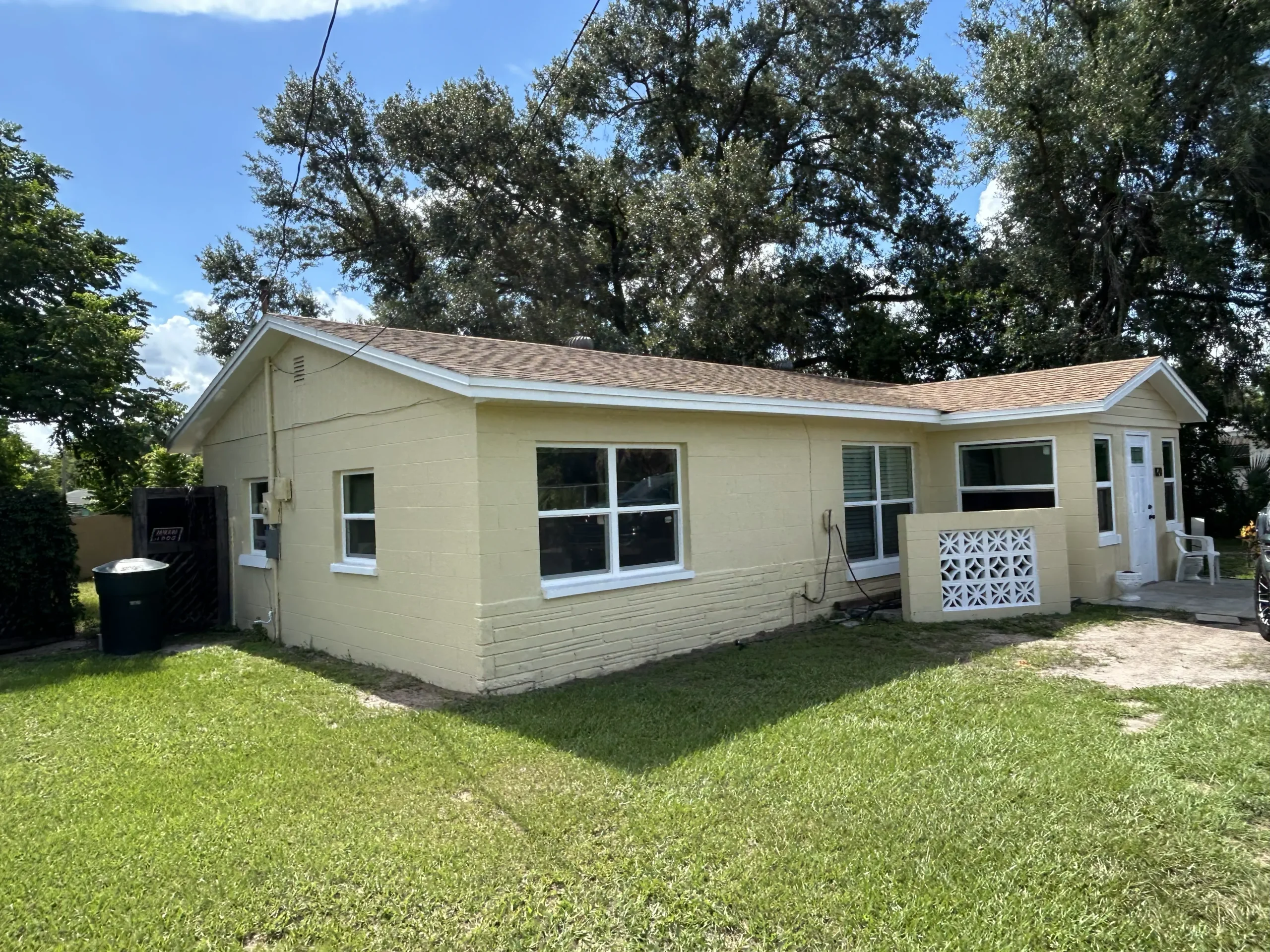 After: the same yellow concrete block home with a new shingle roof, new white windows and trim, and fresh exterior paint after CRA funded rehabilitation
