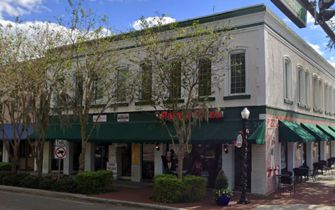 Existing two-story white corner building at Main Street and Broadway with green awnings, currently home to a pizza restaurant